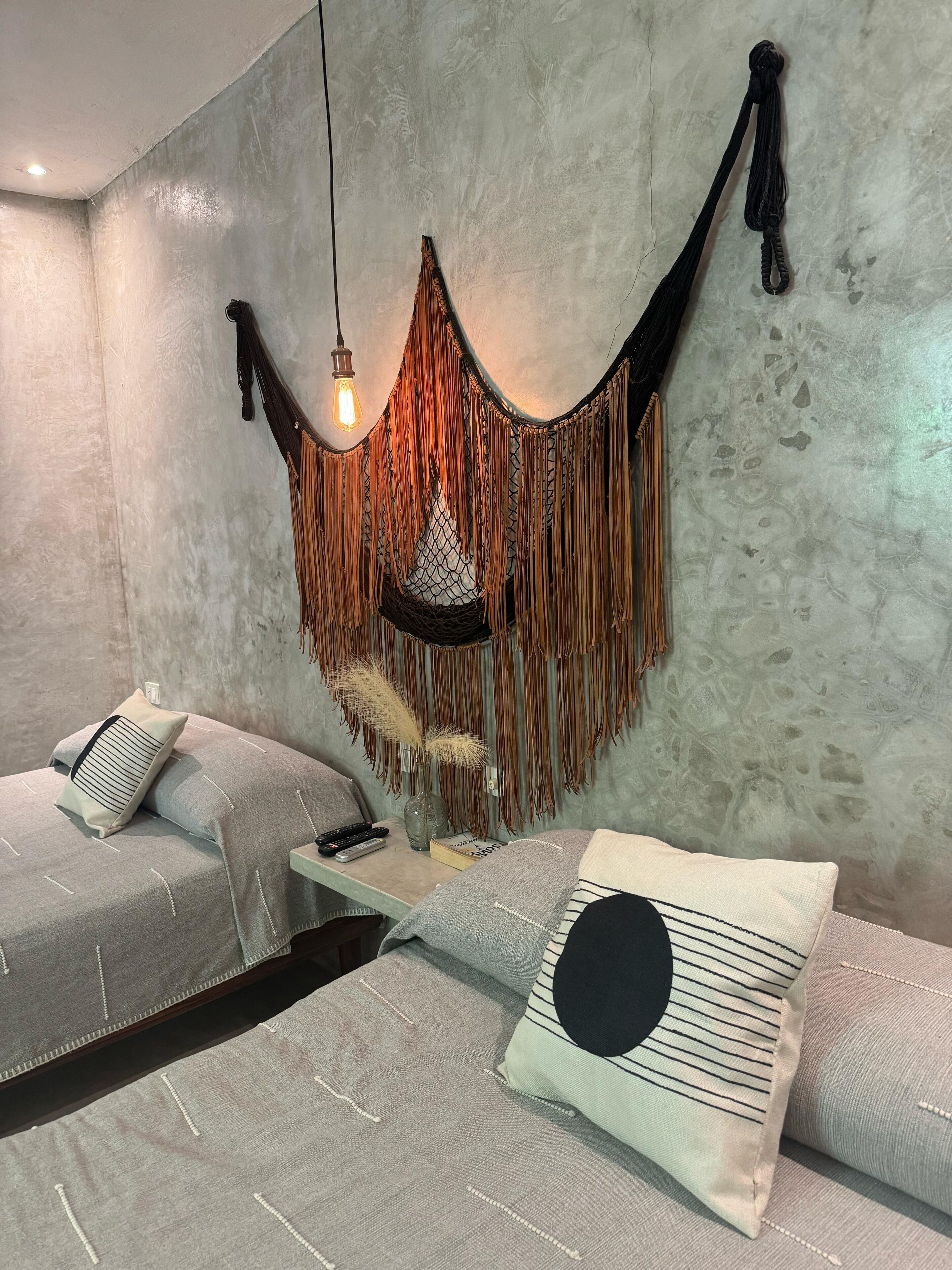 A modern bedroom with a concrete wall, a hanging macrame piece, and a bed with multiple pillows.