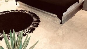 A modern bedroom with a large bed, a round black rug, and a hanging macrame wall decoration. - Apartments & Suites MADRE Holbox Self-Check IN (Isla Holbox)