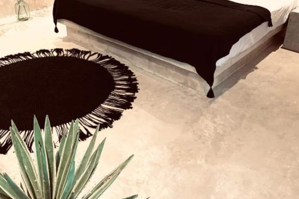 Une chambre moderne avec un grand lit, un tapis rond noir et une décoration murale en macramé suspendue.