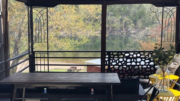 Un espace extérieur aménagé pour prendre les repas, avec vue sur un lac et des arbres.