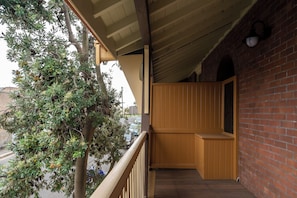 A wooden balcony with a view of a tree and a brick wall.