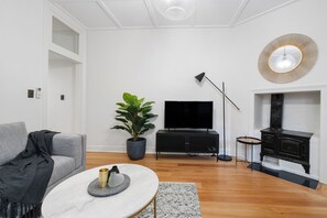 A modern living room with a grey sofa, a round coffee table, a potted plant, a flat-screen TV, a black TV stand, a floor lamp, and a fireplace.
