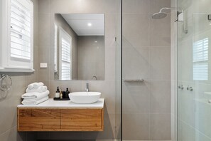 A modern bathroom with a large mirror, a white sink, and a glass shower enclosure.