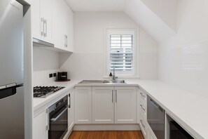 A modern kitchen with white cabinetry, a stainless steel refrigerator, a gas stove, and a window with blinds.