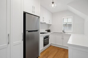 A modern kitchen with white cabinetry, a stainless steel refrigerator, a gas stove, and a built-in oven.
