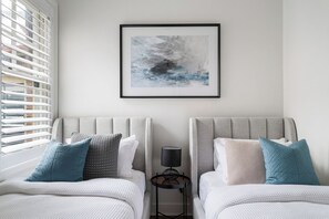 A bedroom with two beds, a framed abstract painting, a side table with a lamp, and a window with blinds. - Harbour View Terrace In The Heart Of The Rocks (Millers Point)