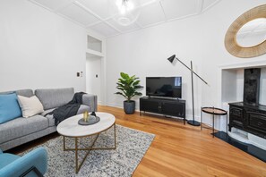 A modern living room with a grey sofa, a round coffee table, a television, a potted plant, a floor lamp, and a fireplace.