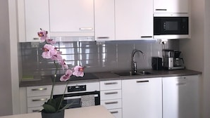 A modern kitchen with white cabinets, a black microwave, and a coffee maker on the countertop. - Kotimaailma Pori Center (Pori)