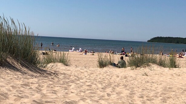 A sandy beach with people sunbathing and swimming. - Kotimaailma Pori Center (Pori)