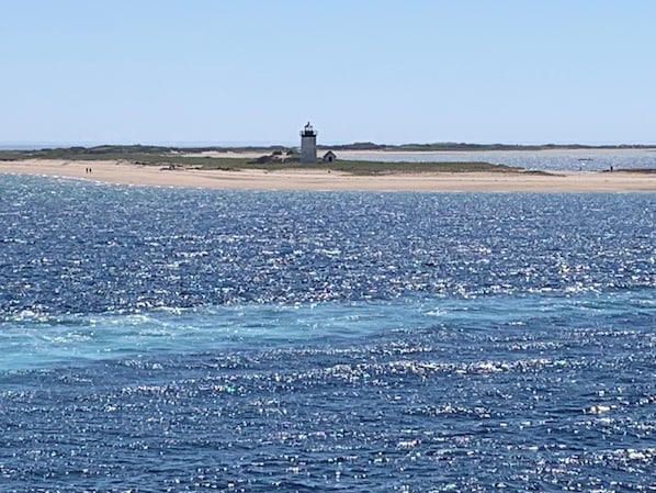 Un paysage côtier avec un phare sur une plage de sable, une mer calme et un ciel dégagé.