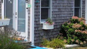 Una casa de un piso con fachada de tejas grises, una puerta blanca y una pequeña zona de porche.