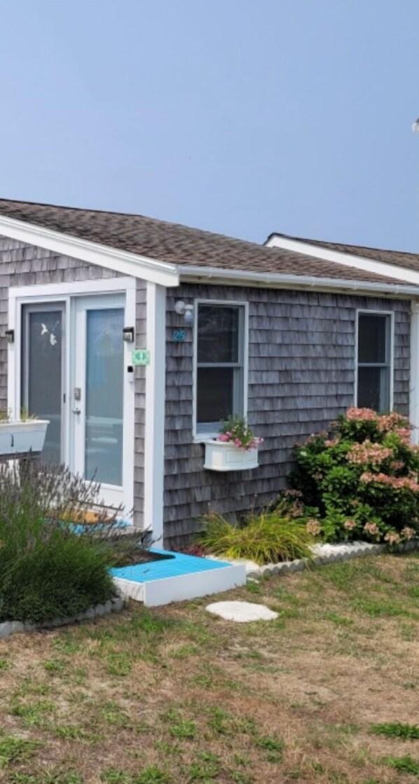 A single-story house with a gray shingled exterior, a white door, and a small porch area.