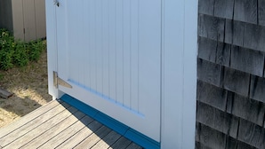 Un portón de madera blanca con detalles azules, un picaporte metálico y una pequeña bolsa azul colgada de un gancho.