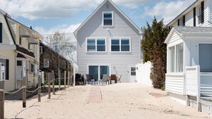 Une propriété située en bord de mer, avec une grande maison blanche, un chemin de sable et une clôture en bois.