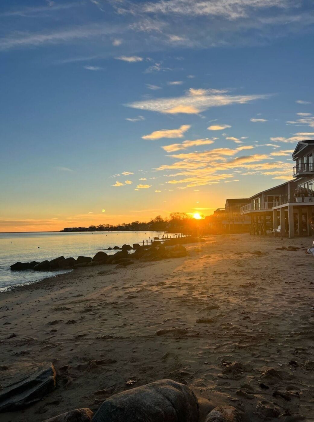 A beach with a sunset, a pier, and buildings in the background.