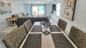 Un salon moderne comprenant un canapé, une table à manger et des chaises, un téléviseur et des œuvres d’art accrochées aux murs.
