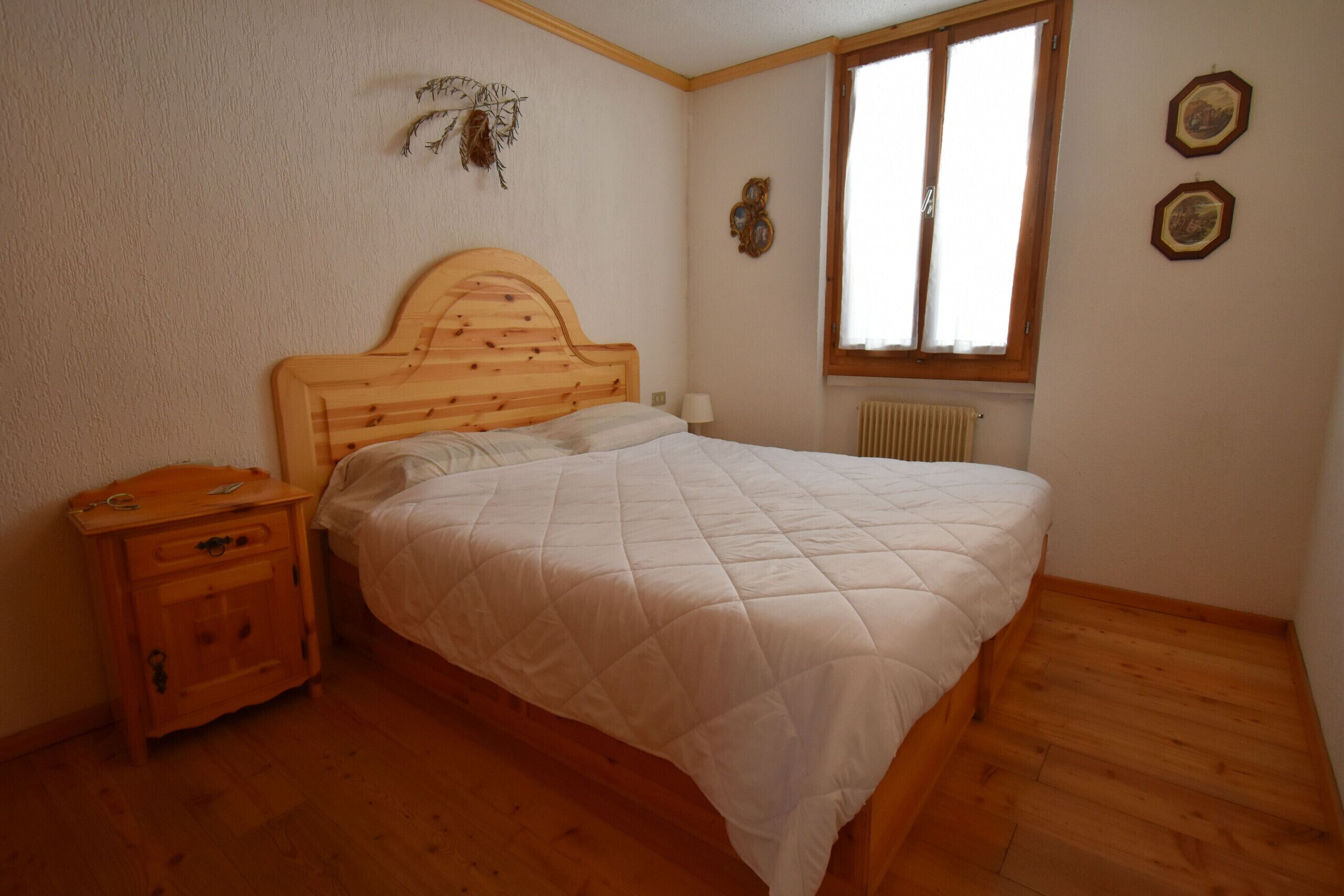 A bedroom with a wooden bed, a nightstand, a window, and wall decorations.