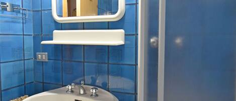 A bathroom with blue tiled walls, a white sink, a mirror, and a shower enclosure.