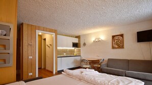 Quarto de hotel com cama, sofá, cozinha compacta e televisão na parede.