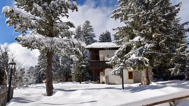 Eine schneebedeckte Lodge mit Holzbalkon und Steinmauer.