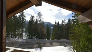 Blick von einem hölzernen Balkon auf eine verschneite Landschaft mit Bäumen und einem Berg im Hintergrund.