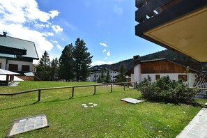 Un espace extérieur verdoyant, avec une rambarde en métal, une clôture en bois et des bâtiments en arrière-plan.