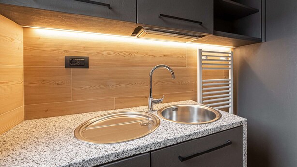 Een keuken met twee roestvrijstalen spoelbakken, een houten spatwand en een moderne kraan.