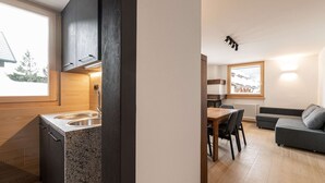 Een moderne keuken met granieten aanrecht, een eethoek met tafel en stoelen, en een woonkamer met bank en raam met uitzicht.