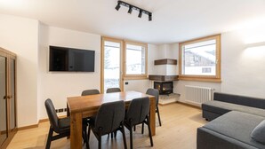 Een moderne woonkamer met een houten eettafel, een grijze bank en een open haard.