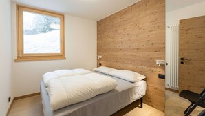 Een slaapkamer met een houten wand, een raam met uitzicht op sneeuw en een radiator.