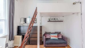 Et værelse med sofa, stige, radiator og et vindue med gardiner.