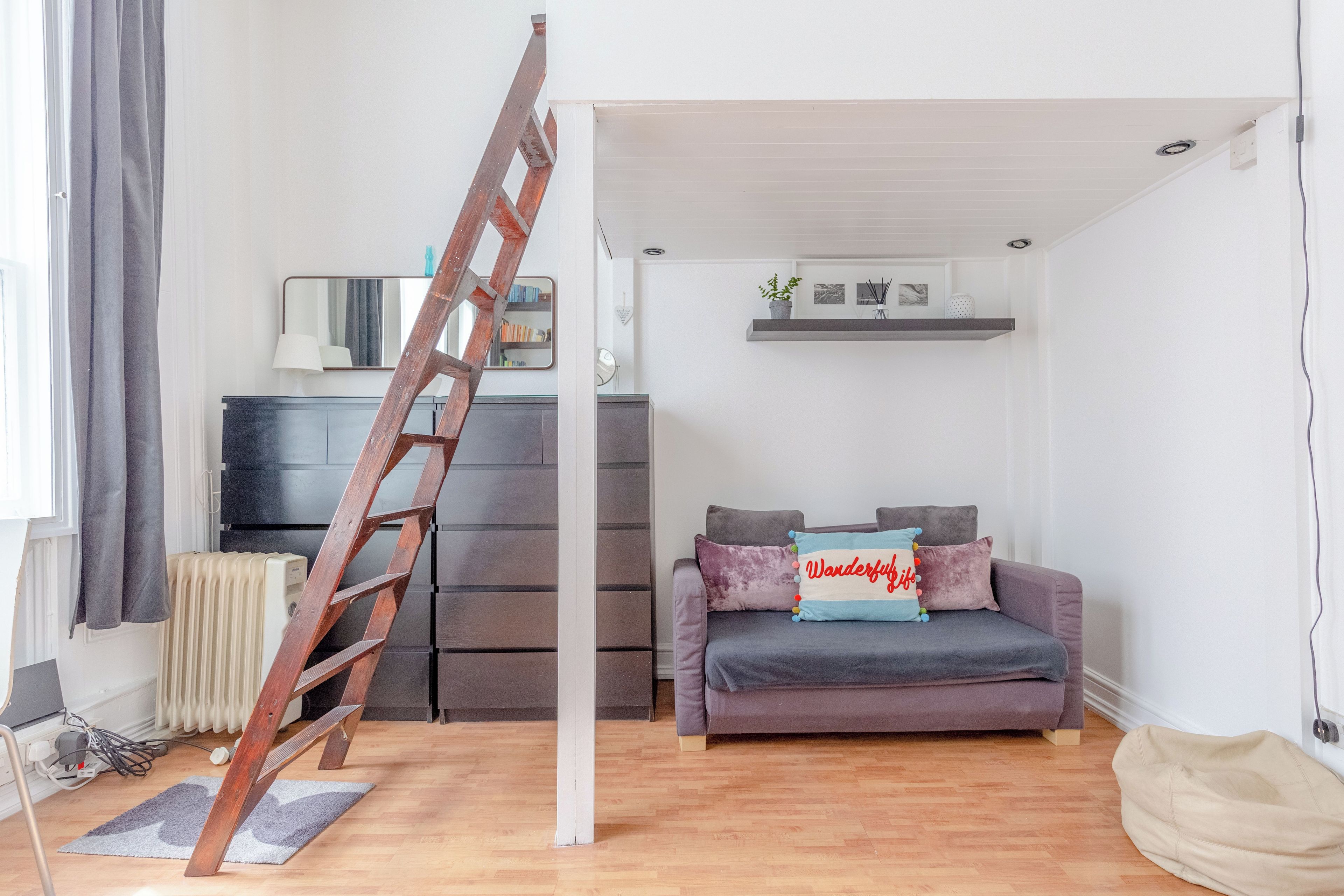 A modern living room with a wooden ladder, a grey sofa, and a small white shelf with decorative items.