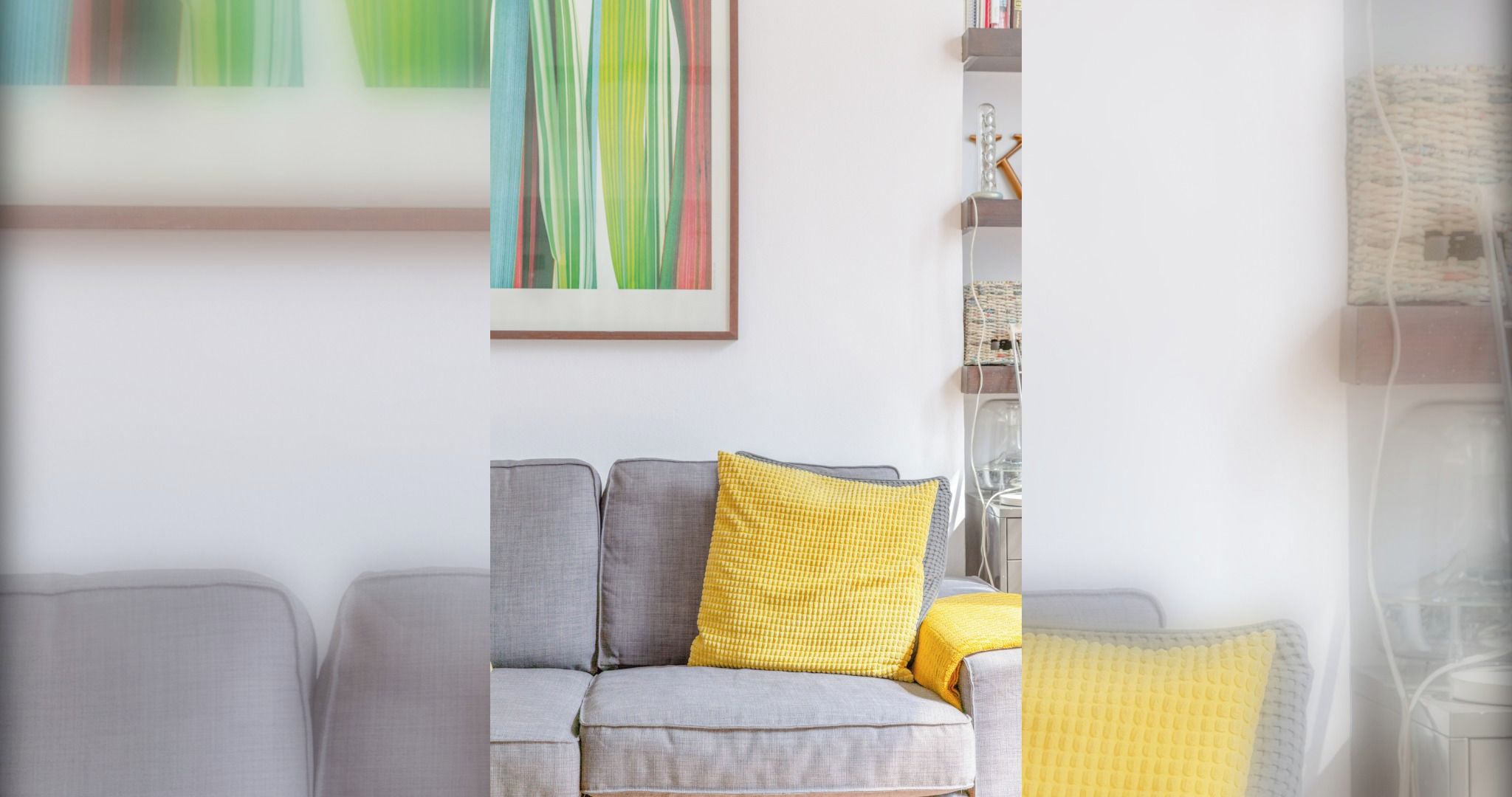 Un salon avec un canapé gris, un coussin jaune et un tableau abstrait encadré accroché au mur.