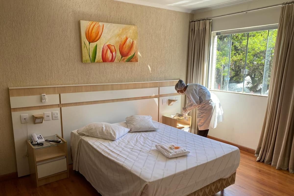 A hotel room with a large bed, a nightstand with a phone and a lamp, a painting of tulips on the wall, and a window with curtains.
