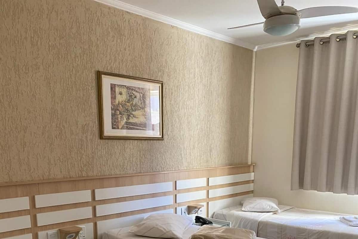 A hotel room with two single beds, a nightstand, a ceiling fan, and a framed picture on the wall.
