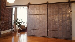 Habitación amplia con un gran ventanal corredera, pared de ladrillo, suelo de madera y lámpara colgante.