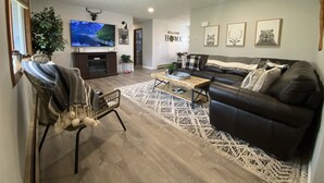 A living room with a fireplace, a black leather sofa, a television, and framed pictures on the wall.