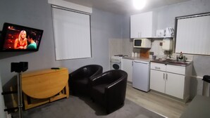 Une cuisine de taille réduite avec des meubles blancs, un four à micro-ondes, une cuisinière et un évier. On y trouve une table en bois et deux chaises noires.