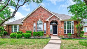 A brick house with a front entrance, a small porch, and a well-maintained lawn.