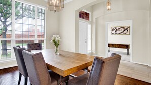 A dining area with a wooden table and upholstered chairs, a vase with flowers, and a chandelier.
