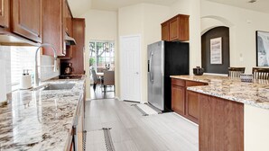 A modern kitchen with wooden cabinets, a stainless steel refrigerator, and a marble countertop.