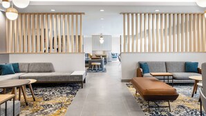 Un moderno vestíbulo de hotel con una zona de estar central, separadores de madera y una alfombra estampada.