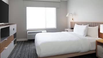 Una habitación de hotel con una cama, televisor, mesita de noche, lámpara y ventana.