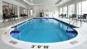 Una piscina interior de 91 centímetros de profundidad, con agua azul cristalina, rodeada de sillas y mesas negras, y grandes ventanales en un lado.