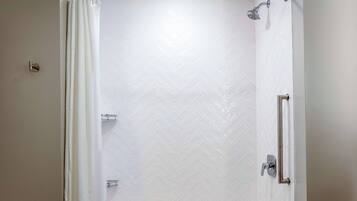 A shower with a white herringbone tile wall, a showerhead, and a curtain rod.