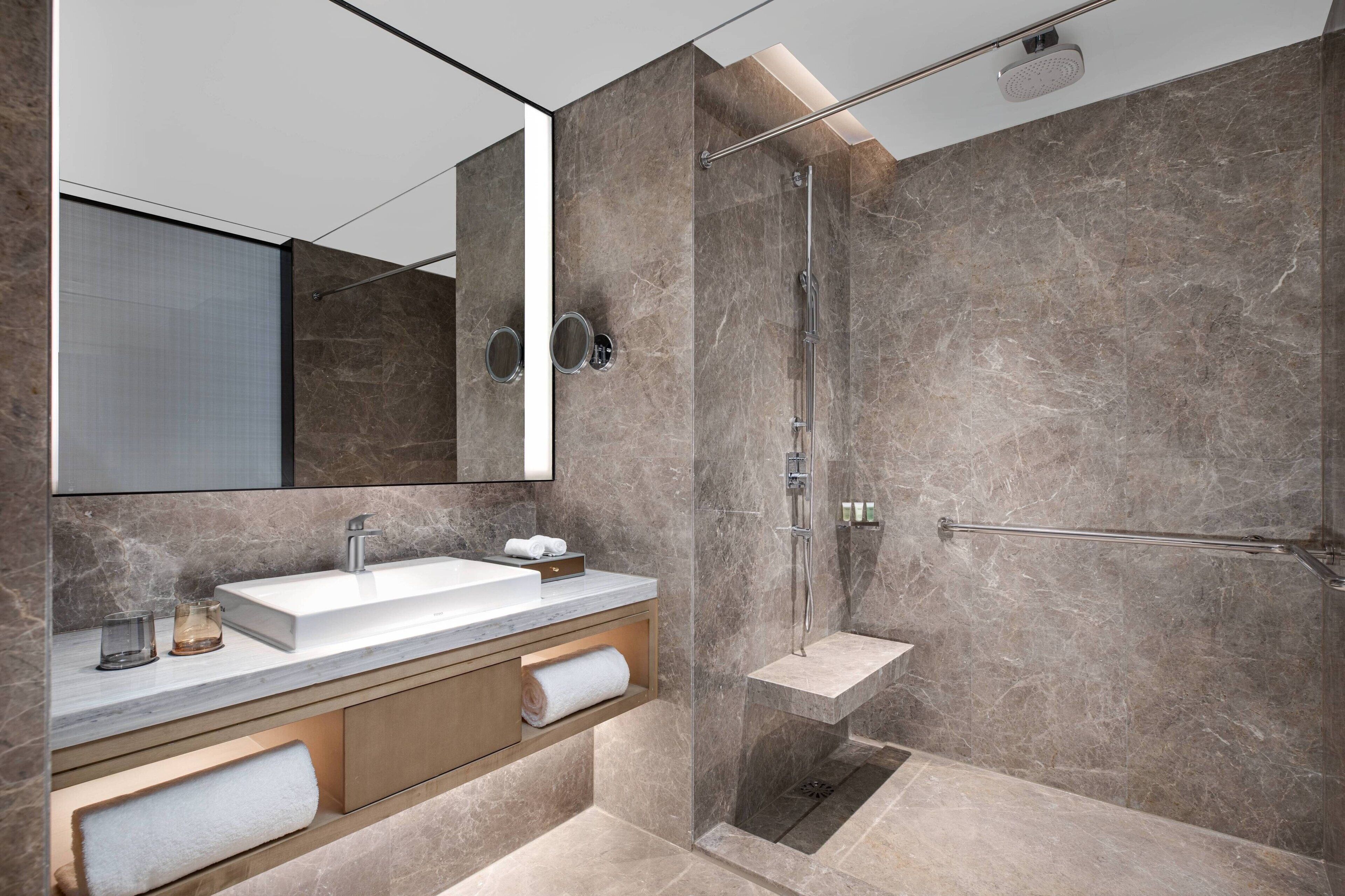 A modern bathroom with a large mirror, a sink, and a walk-in shower.
