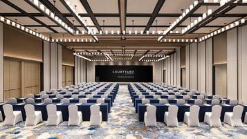Un salón de conferencias con filas de mesas y sillas, una pantalla grande al frente y una alfombra estampada.