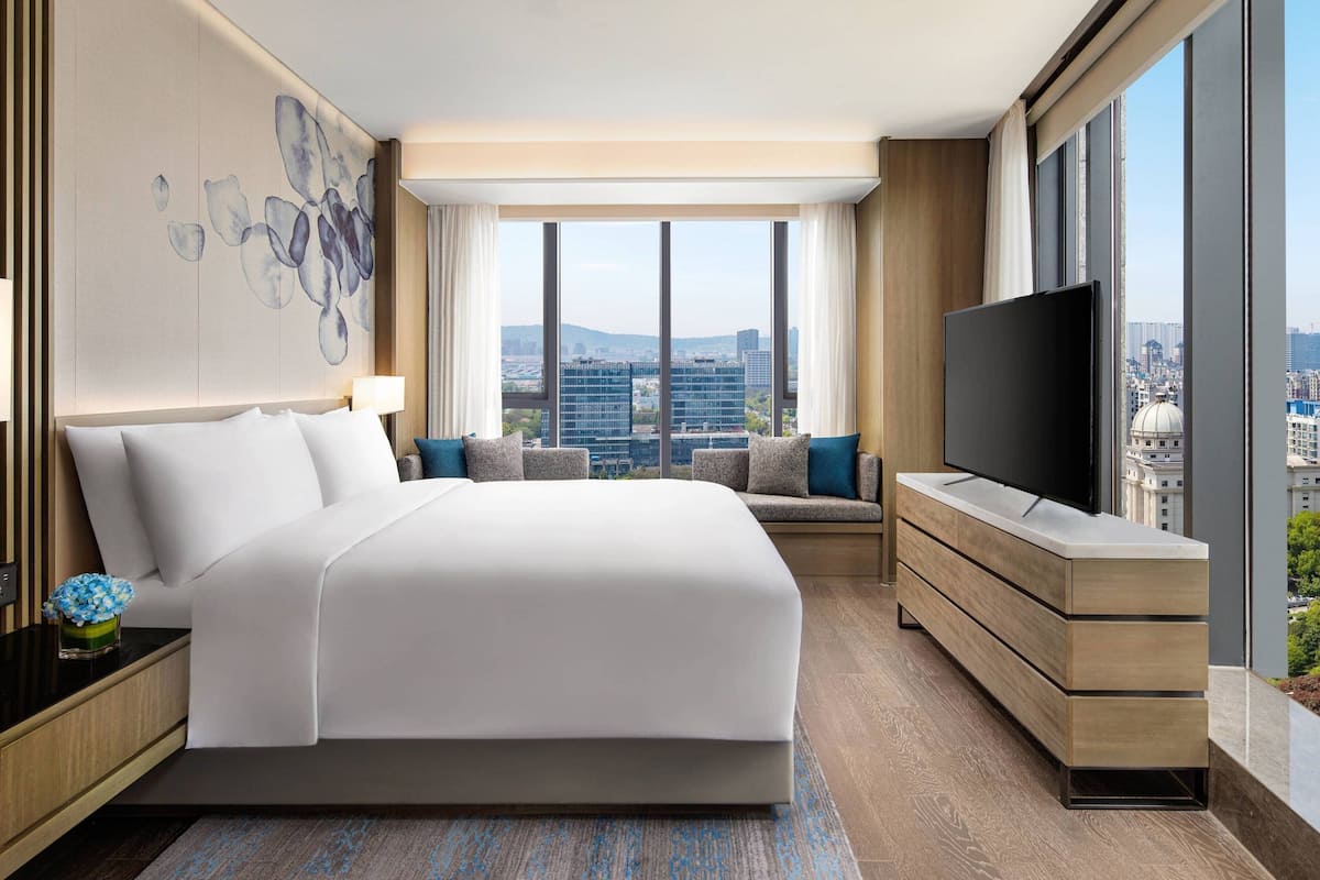 Una habitación de hotel moderna con una cama grande, televisión, sofá y vista a la ciudad.