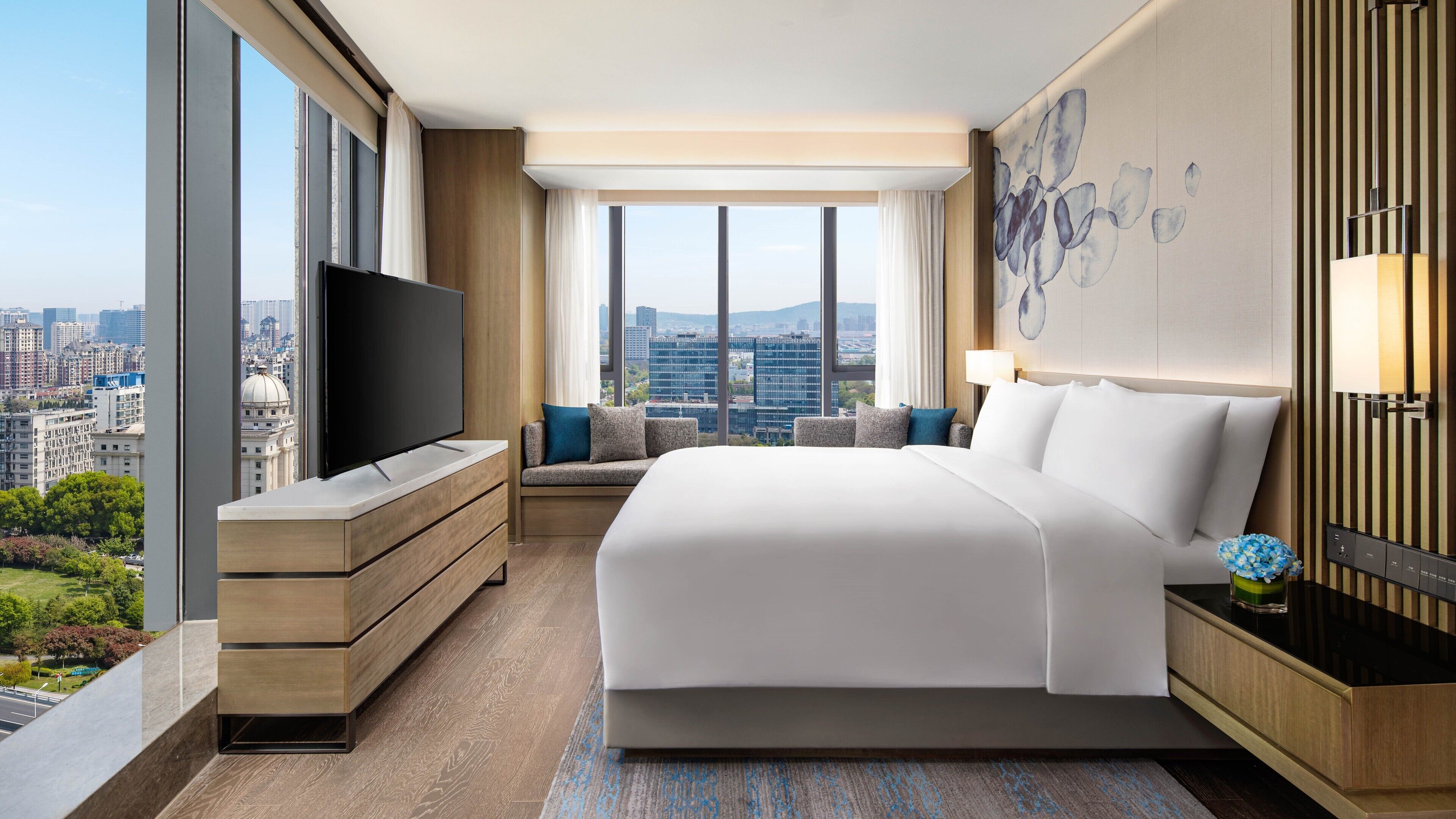 Una habitación de hotel moderna con una cama grande, televisor, escritorio y vistas a la ciudad.
