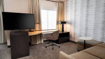 A hotel room with a flat-screen TV, a desk with a chair, a sofa, a small table, and a patterned wall.